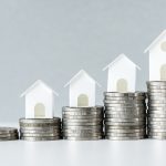Imagem de quatro pequenas casas brancas de papel posicionadas sobre pilhas de moedas de prata, organizadas em ordem crescente da esquerda para a direita. A cena simboliza o crescimento e valorização dos investimentos em fundos imobiliários, destacando o potencial de rentabilidade nesse tipo de aplicação financeira.