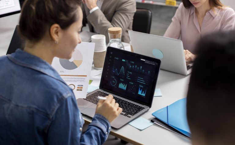 Início 20 Equipe de profissionais reunida em escritório, analisando gráficos e indicadores financeiros em telas de notebook e relatórios impressos. A cena destaca o uso de inteligência artificial para interpretação de dados e apoio na tomada de decisões estratégicas em ambientes corporativos.